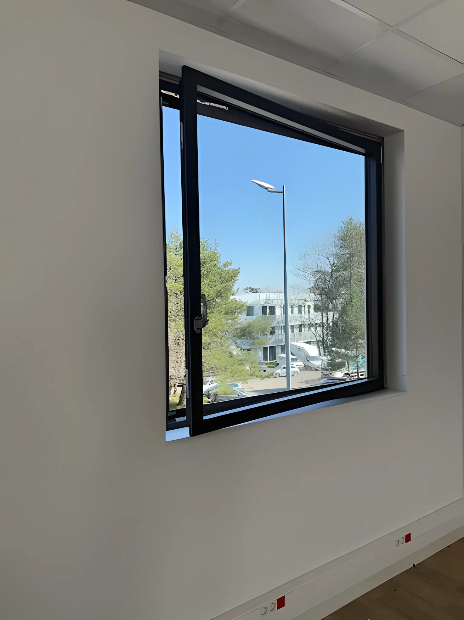 Fenêtre aluminium noire basculée en soufflet dans un mur blanc